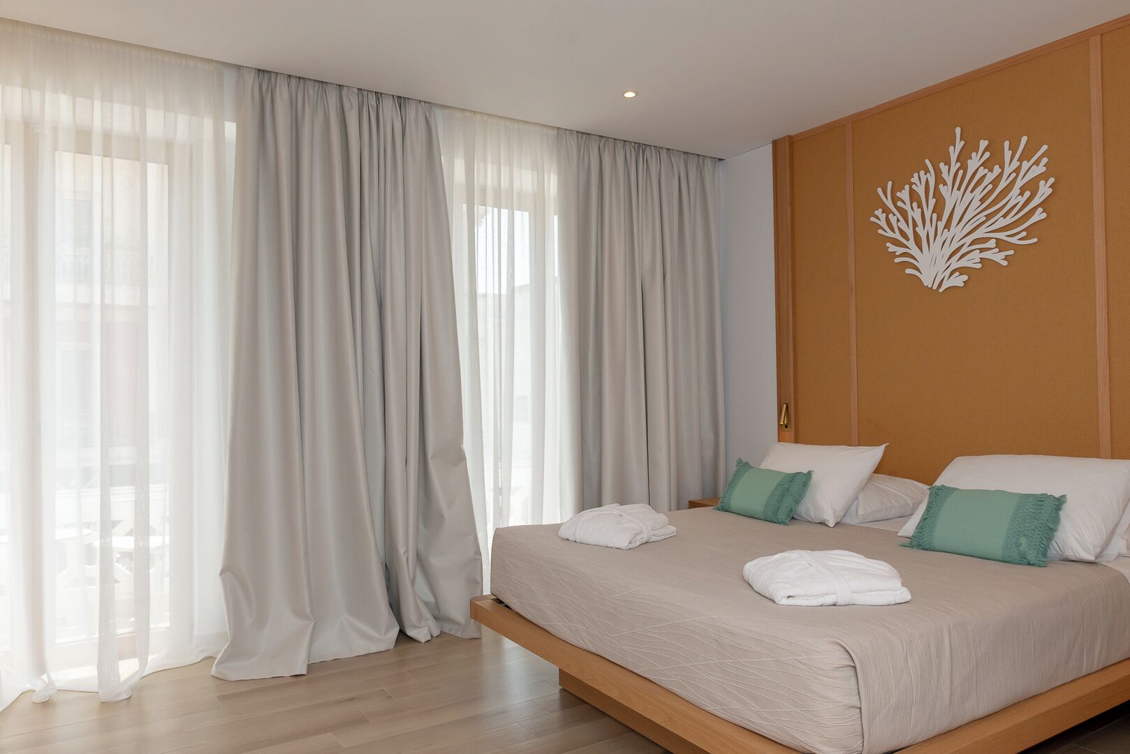 A modern hotel room with a large bed, sheer curtains, and a decorative wall piece.