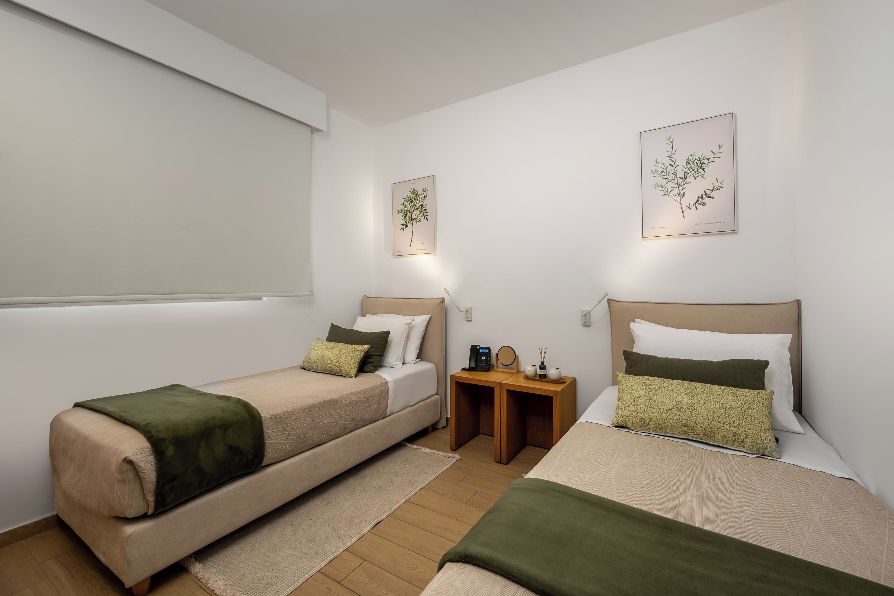 Quarto com duas camas de solteiro, uma mesa de cabeceira com abajur e uma obra de arte na parede.