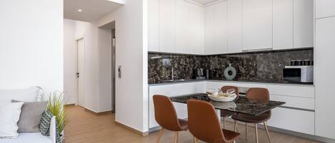 Una cocina moderna con armarios blancos, salpicadero de mármol y un comedor con mesa negra y sillas marrones.
