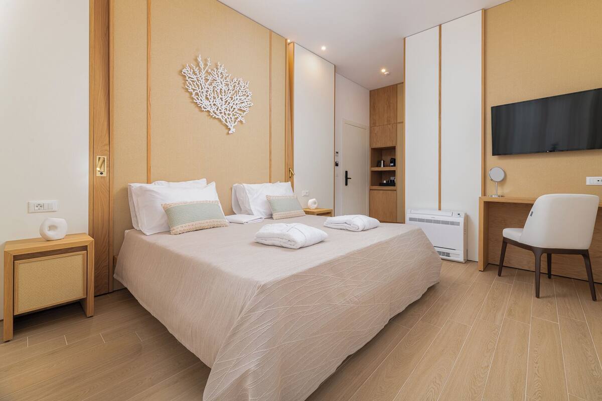 A modern hotel room with a large bed, a desk with a chair, a flat-screen TV, and a wall-mounted decorative piece.