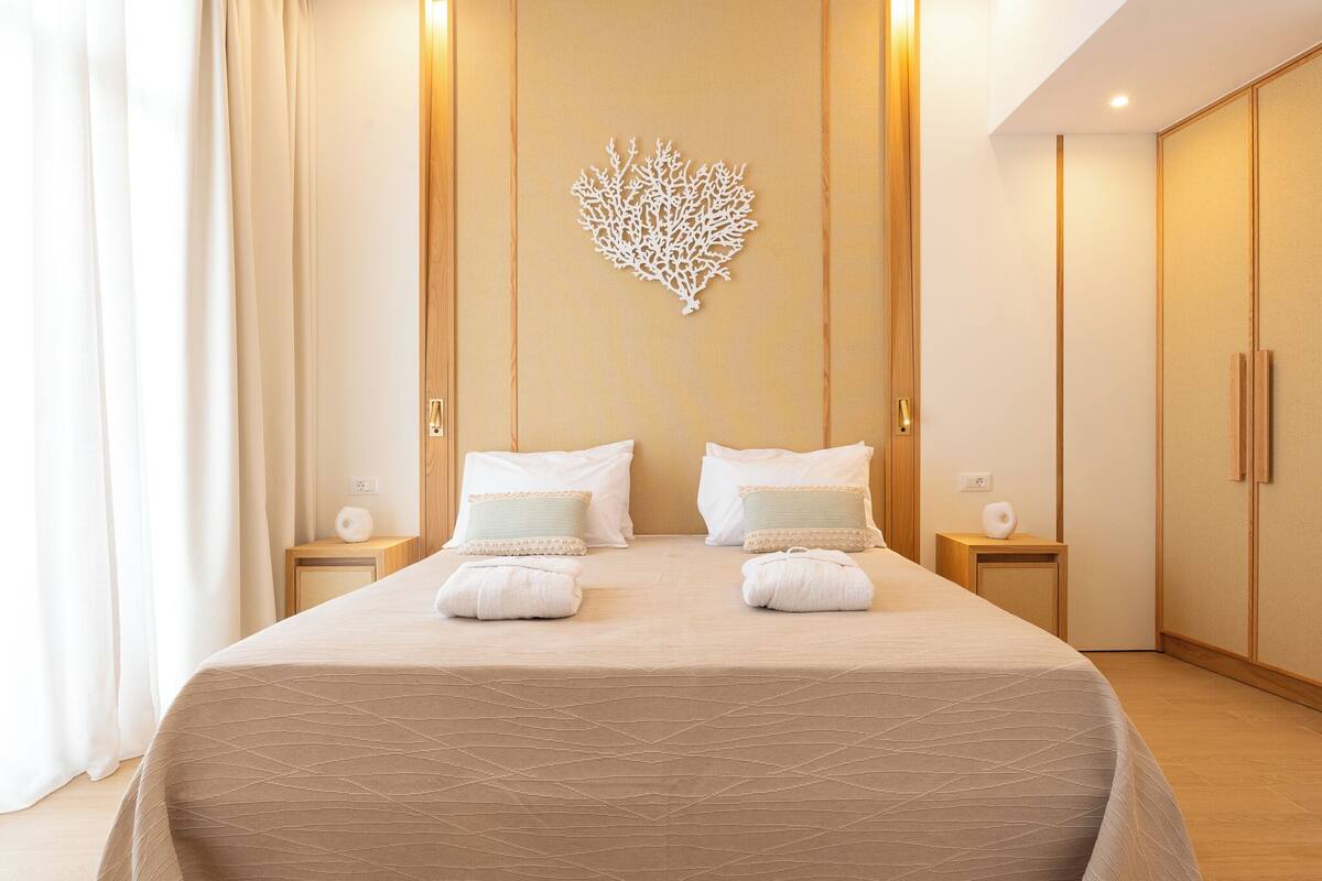 A hotel room with a large bed, two bedside tables, a decorative wall piece, and wooden wardrobes.