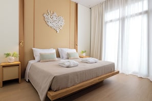 A modern bedroom with a bed, nightstands, a decorative wall piece, and a view through sheer curtains. - The 12th City Hotel  (Rhodes)