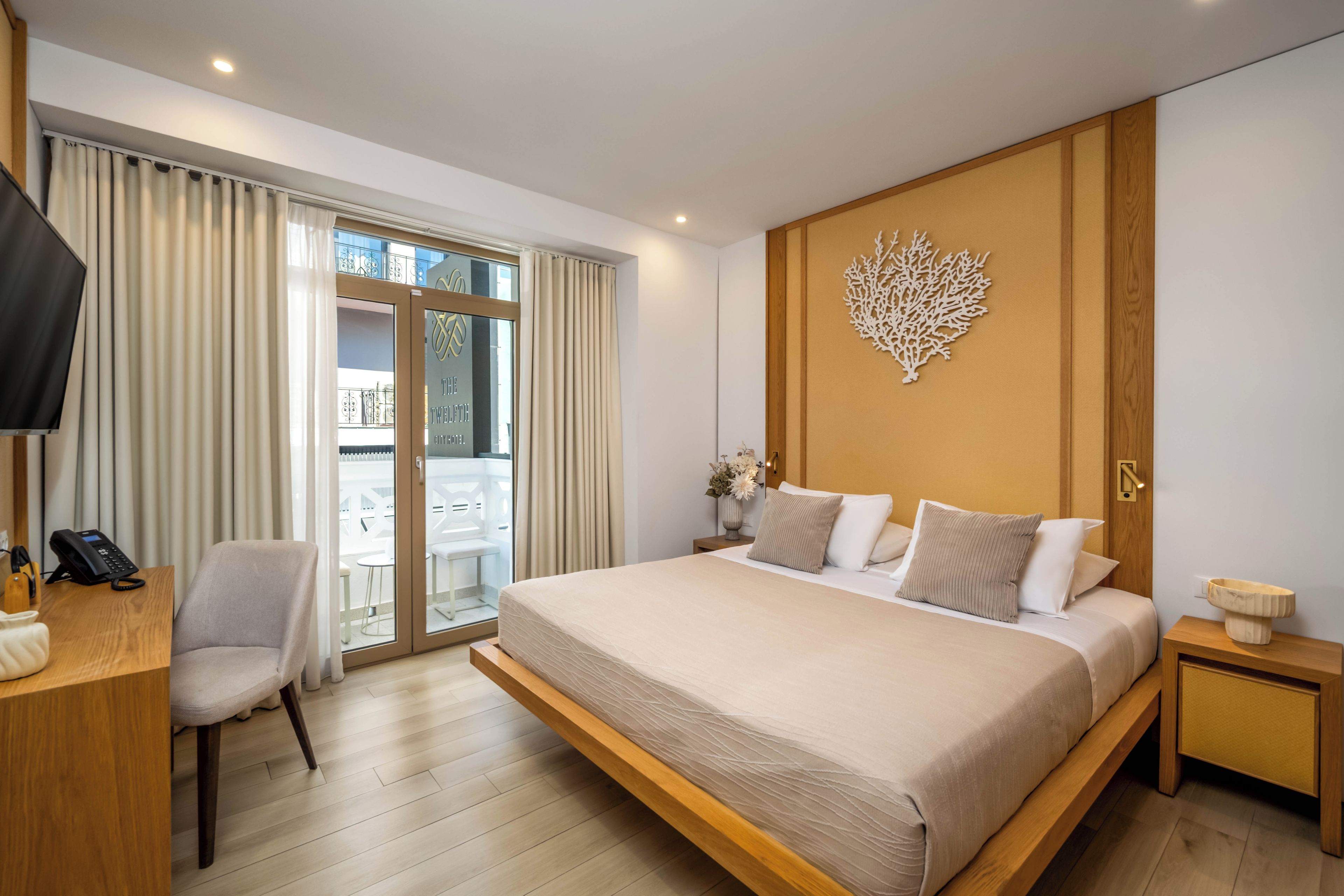Una habitación de hotel con una cama grande, un escritorio con teléfono, una silla, una mesita de noche con lámpara y un adorno en la pared.