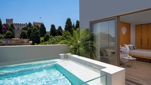 A modern hotel room with a glass wall, a small pool, and a view of a castle. - The 12th City Hotel  (Rhodes)