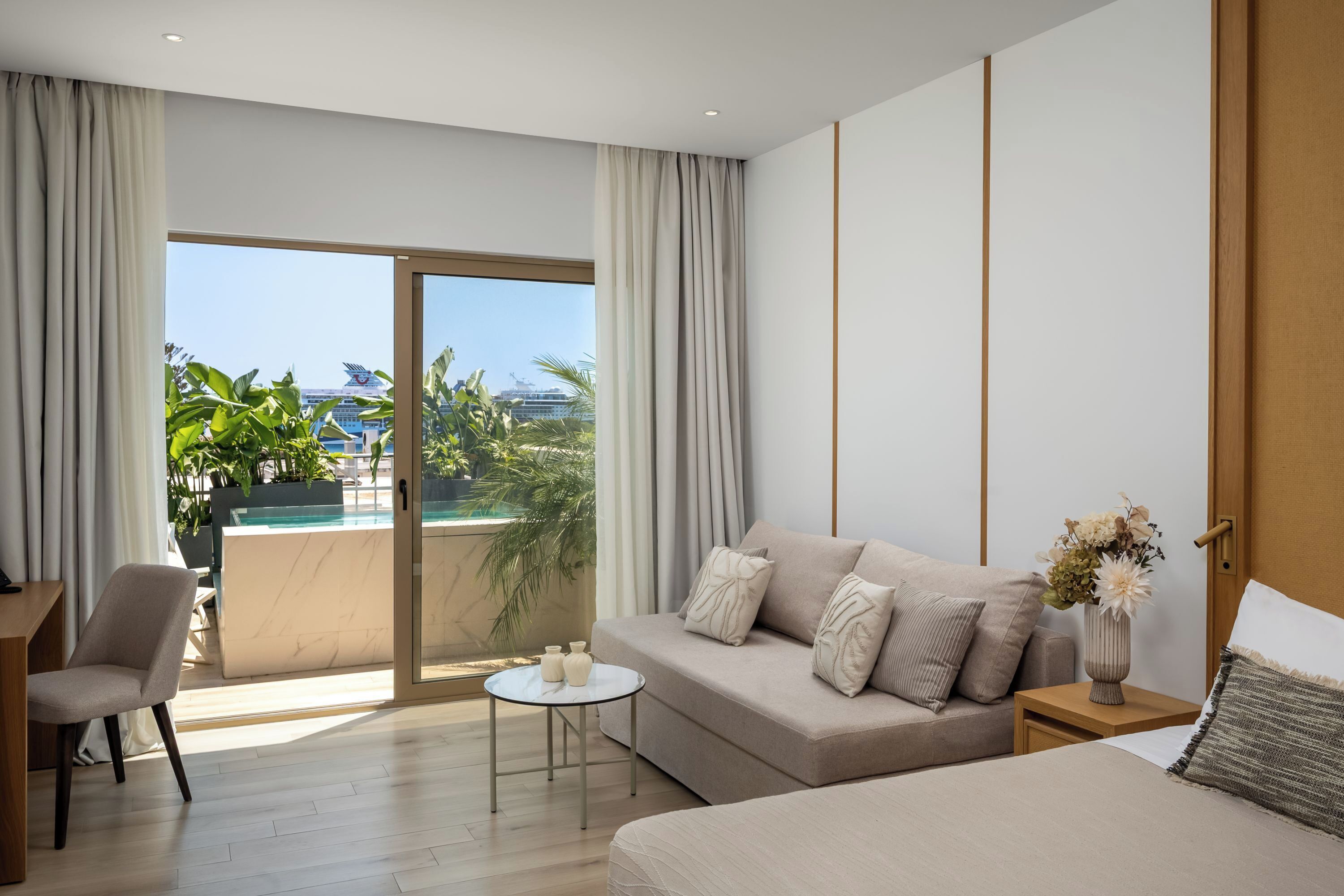 A modern hotel room with a balcony, a sofa, a small table, and a bed.