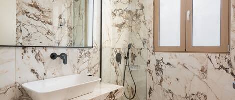 A bathroom with a marble sink, a mirror, and a shower enclosure.