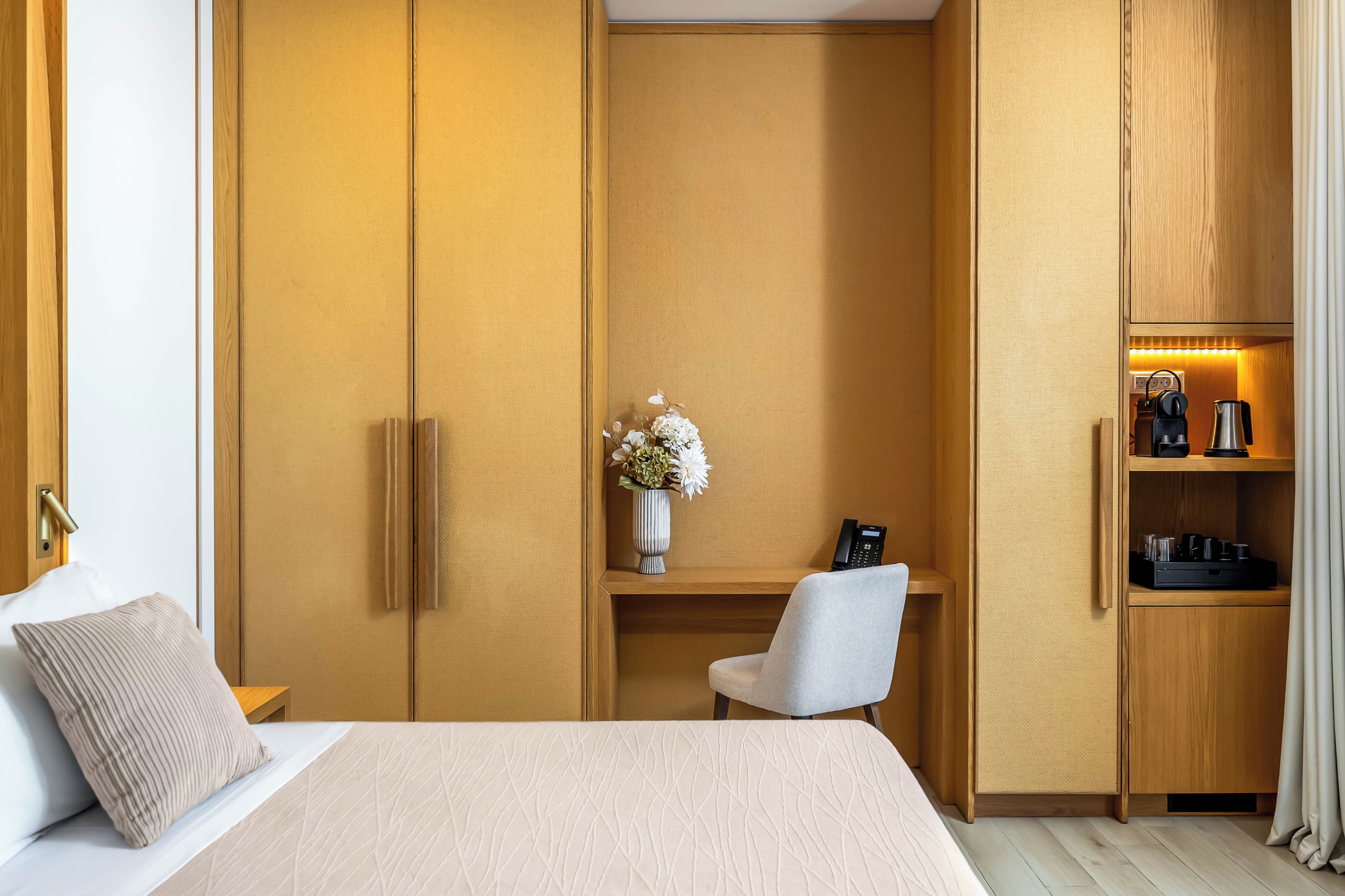 Ett hotellrum med en säng, ett skrivbord, en stol, en garderob och en hylla med diverse bekvämligheter.