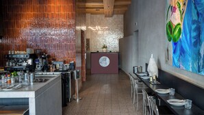 A restaurant with a bar area, a counter with a logo, and a large painting on the wall. - The 12th City Hotel  (Rhodes)