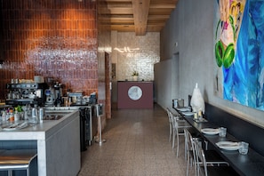 A restaurant with a bar area, a counter with a logo, and a large painting on the wall. - The 12th City Hotel  (Rhodes)