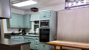 Eine Küche mit hellblauen Schränken, einem Holztisch und einer Bank. Ein Mikrowellenherd und ein Backofen sind vorhanden.