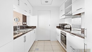 Een moderne keuken met witte kasten, een granieten aanrechtblad, een ingebouwde oven en een roestvrijstalen koelkast.