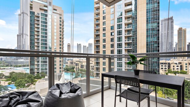 Een balkon met een tafel en stoelen, met uitzicht op een stadsgezicht met hoogbouw en een zwembad.