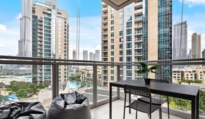 Een balkon met een tafel en stoelen, met uitzicht op een stadsgezicht met hoogbouw en een zwembad.