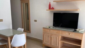 Un espacio habitable compacto con una mesa de comedor, un televisor sobre un mueble de madera, un espejo y un estante con adornos.