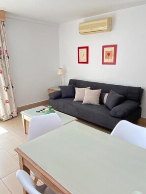 Een woonkamer met een donkergrijze bank, twee ingelijste foto's, een klein tafeltje en een lamp.