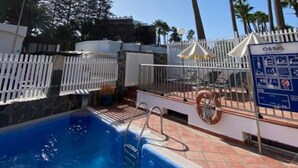 Una piscina con valla blanca, palmeras y un letrero que dice "OASIS".