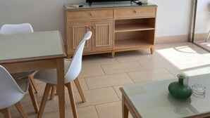Una habitación con un escritorio de madera, un televisor y una zona de comedor con sillas.