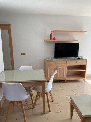 Een kamer met een houten kast, een televisie en een tafel met glazen blad en stoelen.