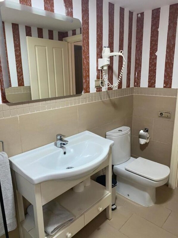 Un baño con lavamanos blanco, inodoro y secador de pelo en la pared.