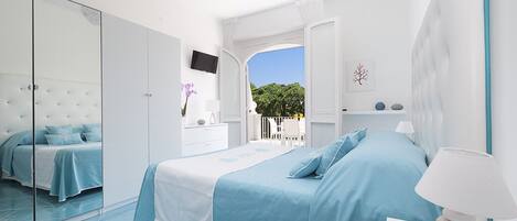 Un dormitorio moderno con una cama grande, un televisor y un balcón con vistas a zonas verdes.