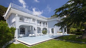 Un edifici gran i blanc de dues plantes, amb piscina, zona de seients a l'aire lliure i un jardí ben cuidat.