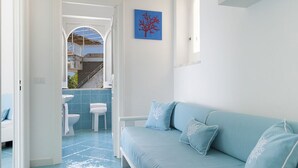 Habitació amb un sofà blau, una porta blanca que condueix a un bany i una paret blava amb un quadre d'un arbre.