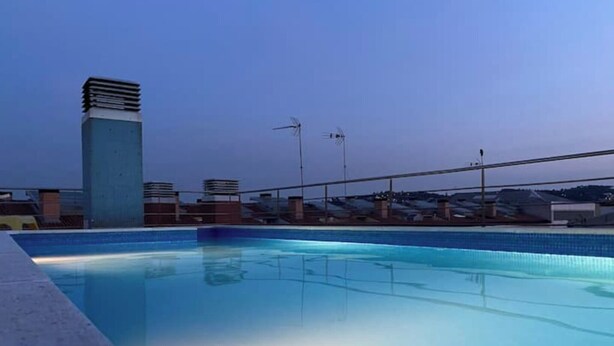 Une piscine à l’eau d’un bleu limpide, entourée d’une terrasse en béton et d’une rambarde en métal.