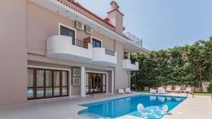 A modern two-story house with a swimming pool, outdoor seating, and a well-maintained garden. - Inviting Villa in Anavissos With Communal Pool (Saronikos)