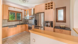 A modern kitchen with wooden cabinets, stainless steel appliances, and a large window. - Inviting Villa in Anavissos With Communal Pool (Saronikos)