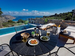 Un espace de restauration en plein air avec piscine, offrant une vue panoramique sur la mer et les collines.