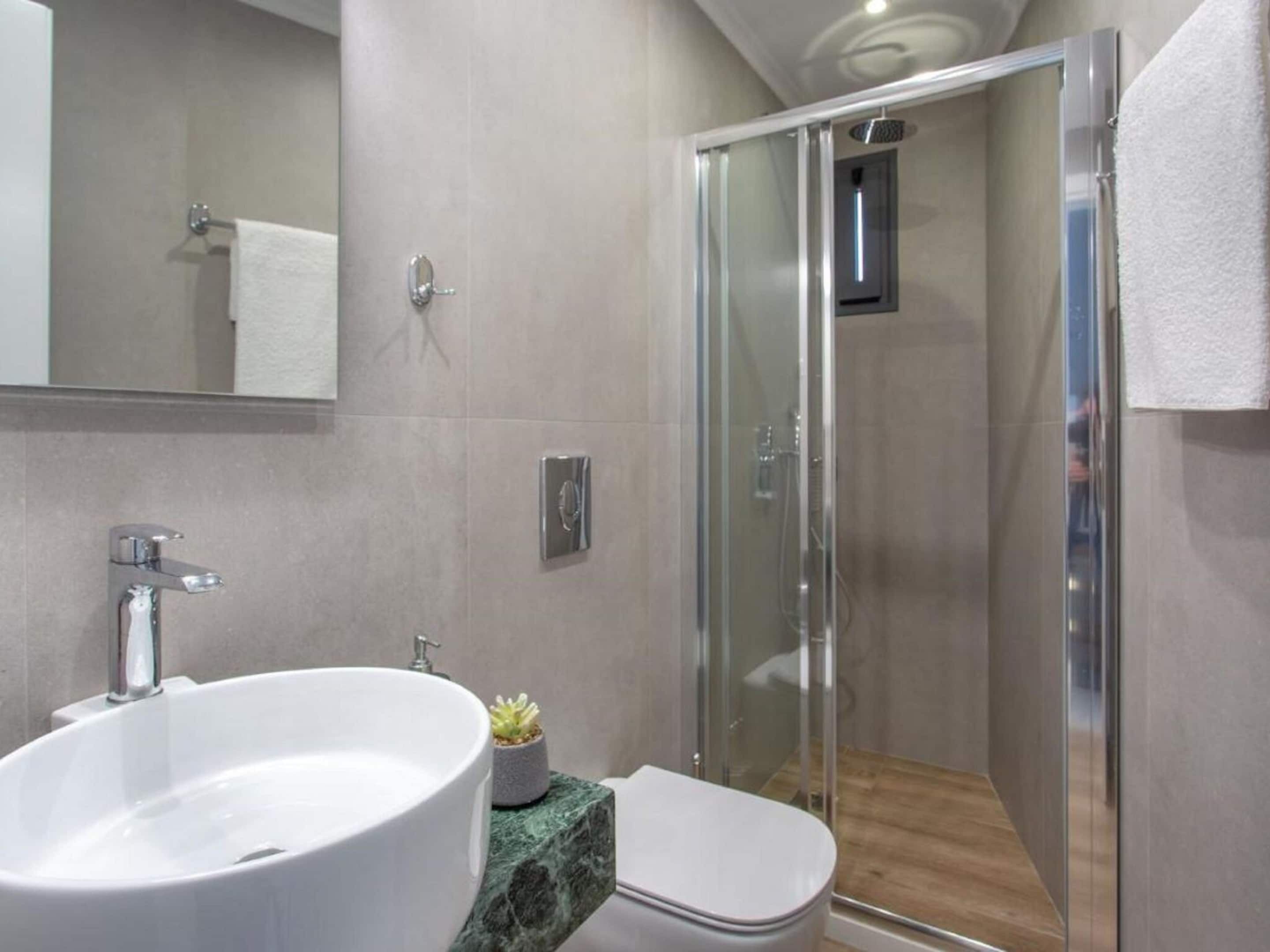 A modern bathroom with a glass shower enclosure, a white sink, and a marble countertop.