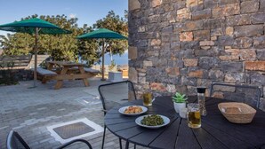An outdoor dining area with stone walls, wooden tables, and green umbrellas. - Mesmerising Villa in Plaka Elounda With Pool (Agios Nikolaos)