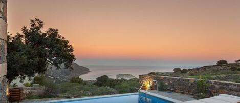 A swimming pool with a sunset view, a lounge chair, and a stone wall.