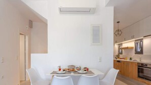 A modern kitchen with white cabinets, a built-in oven, and a dining area with a white table and chairs. - Mesmerising Villa in Plaka Elounda With Pool (Agios Nikolaos)