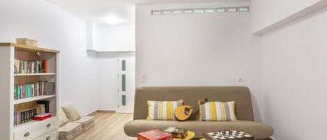 A living room with a sofa, a bookshelf, and two small tables with board games.