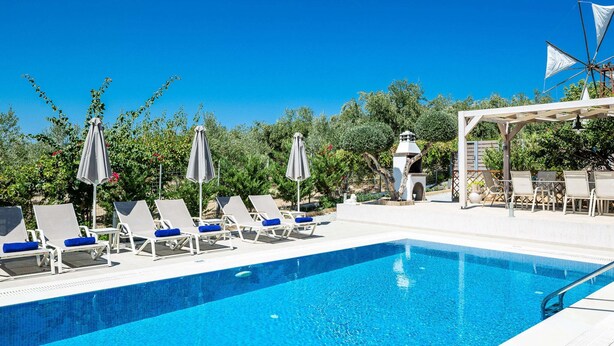 A swimming pool with lounge chairs and umbrellas, surrounded by greenery. - Villa in Crete With Stunning Views & Privacy (Rethymno)
