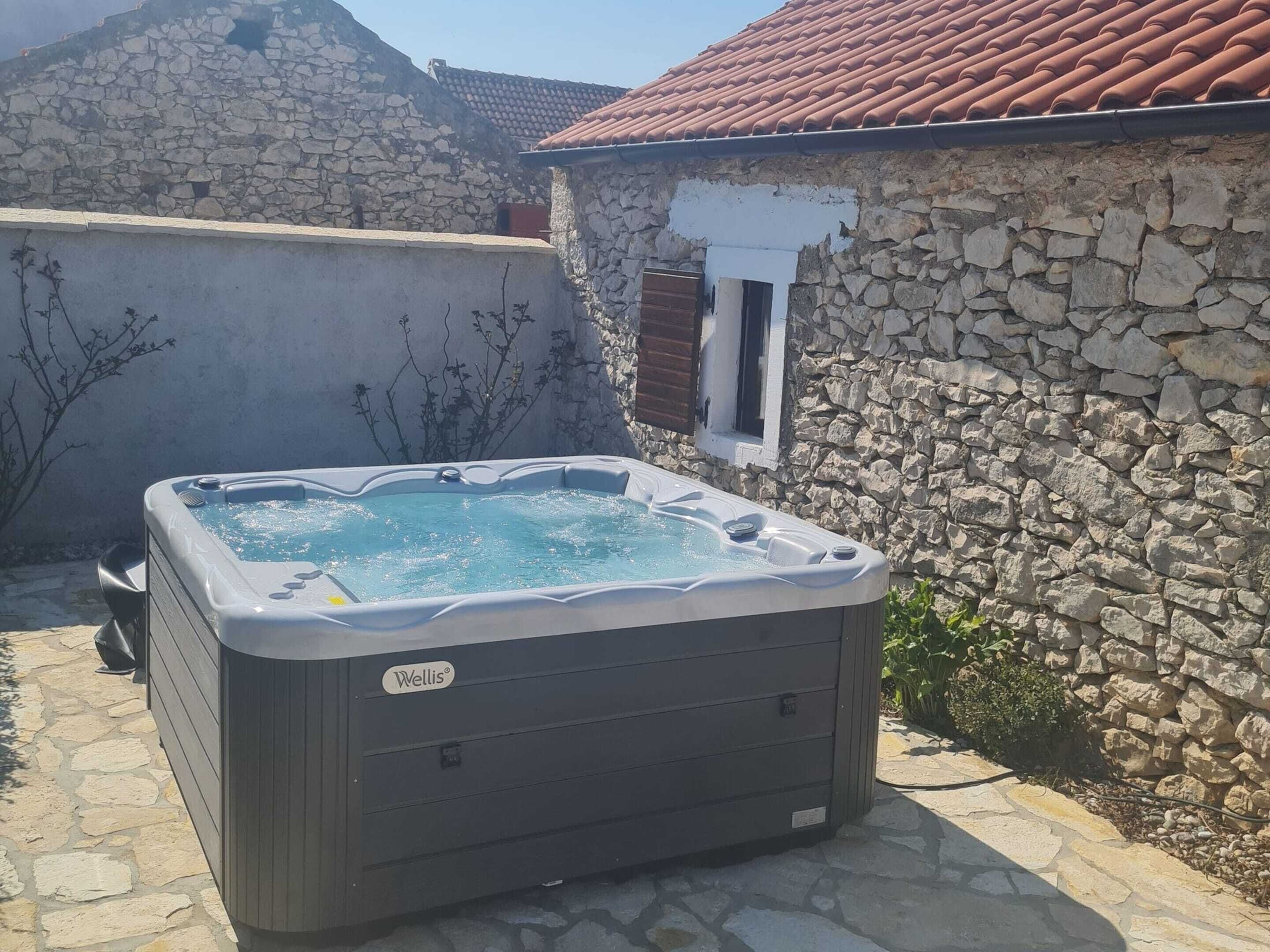 A hot tub in an outdoor setting with stone walls and a tiled roof.