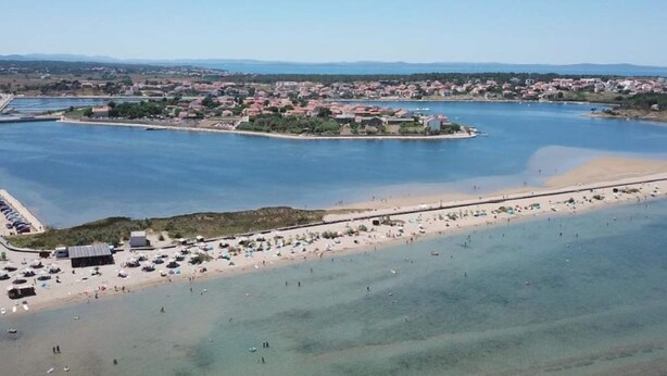 An aerial view of a coastal area with a beach, a marina, and a small island with buildings. - Home With Swimming Pool & Outdoor Kitchen (Nin)