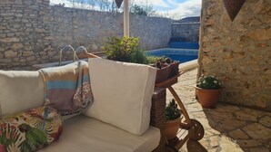 A sunlit patio with a stone wall, a pool, and outdoor furniture. - Home With Swimming Pool & Outdoor Kitchen (Nin)