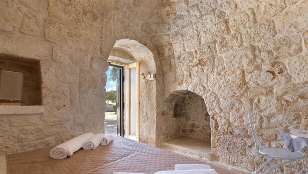 A stone-walled room with a bed, a small table, and a fireplace. - 737 Trulli con Piscina ad Ostuni (Ostuni)