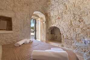 Una habitación de paredes de piedra con una cama, una mesita y una chimenea.