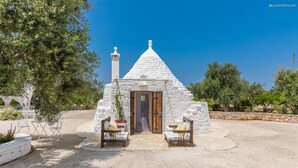 A stone house with a conical roof, a wooden door, and two wooden benches with cushions. - 737 Trulli con Piscina ad Ostuni (Ostuni)