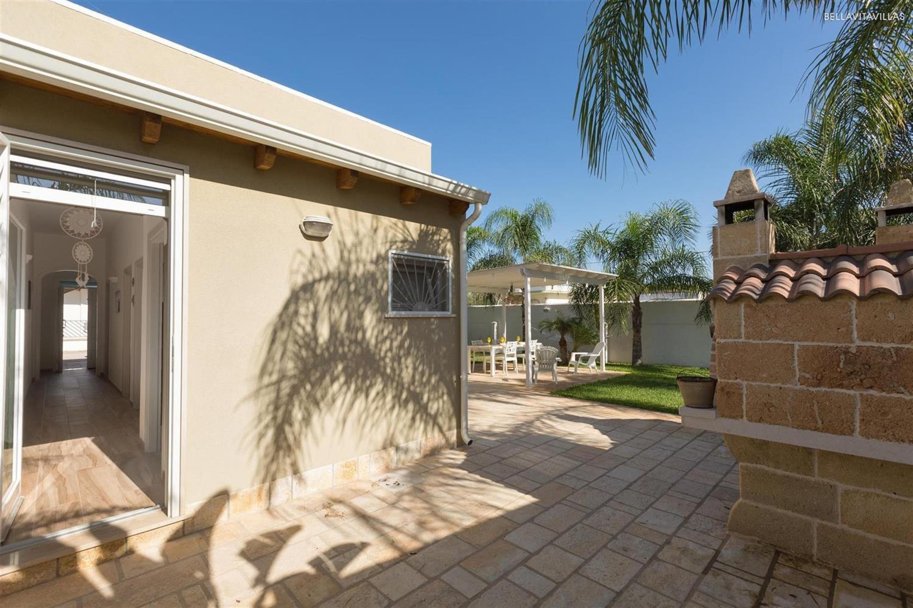 A residential property with a patio area, a covered outdoor seating area, and a view of palm trees.