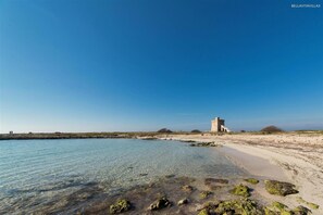 A coastal landscape with clear water, a sandy beach, and a historical stone structure. - 1184 Villino Delle Orchidee Ovest (Nardò)