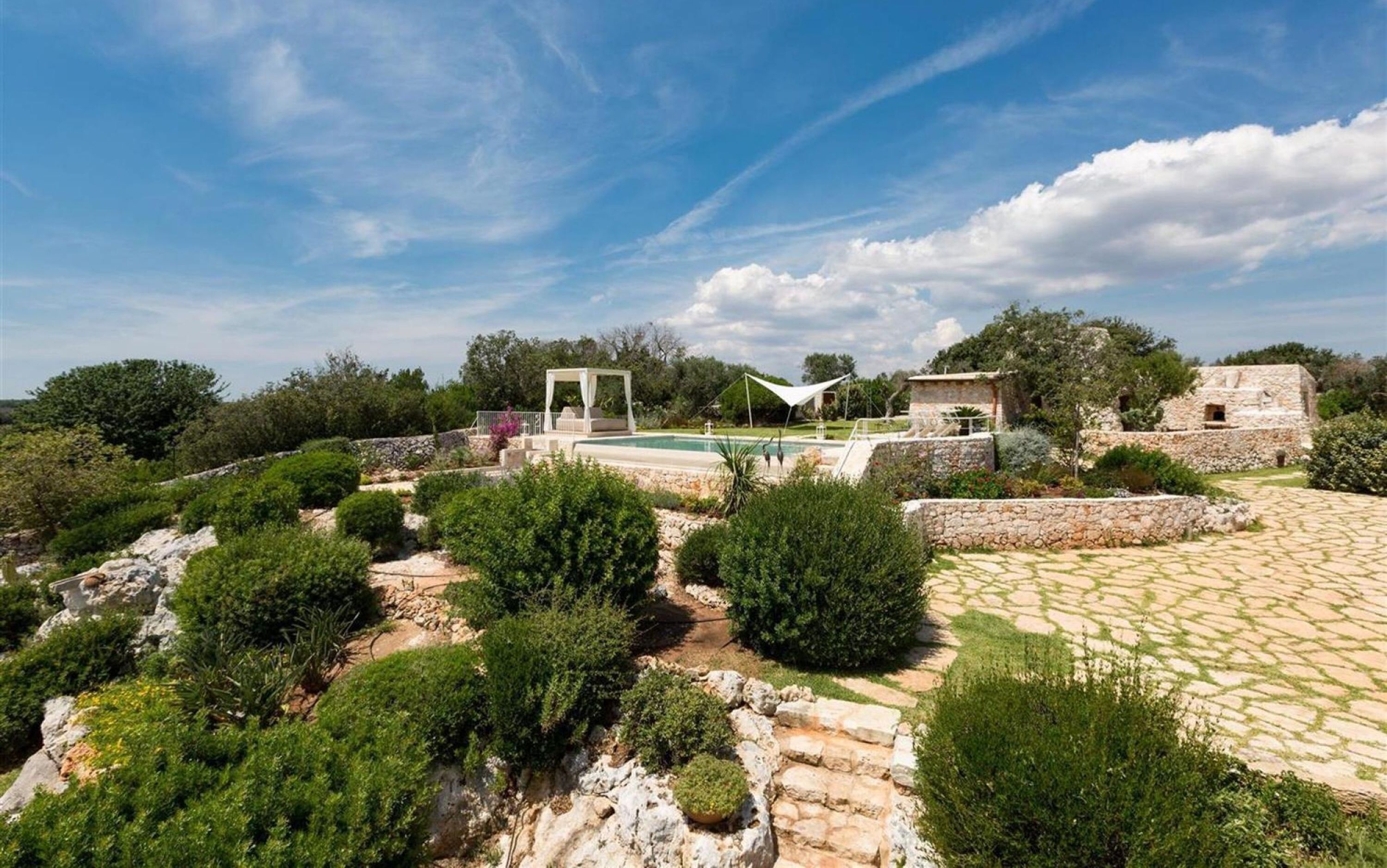 A landscaped garden with a pool, stone structures, and a pergola.