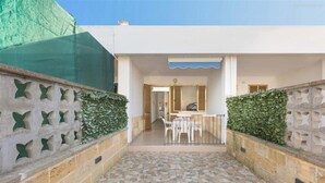 A courtyard with a tiled floor, a dining area with chairs and a table, and a covered seating area with a blue awning.