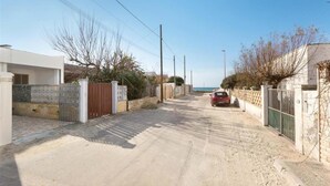 A residential street with houses on both sides, a red car parked on the right, and a clear sky.