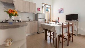 A compact kitchen with a dining area, a refrigerator, a stove, and a television.