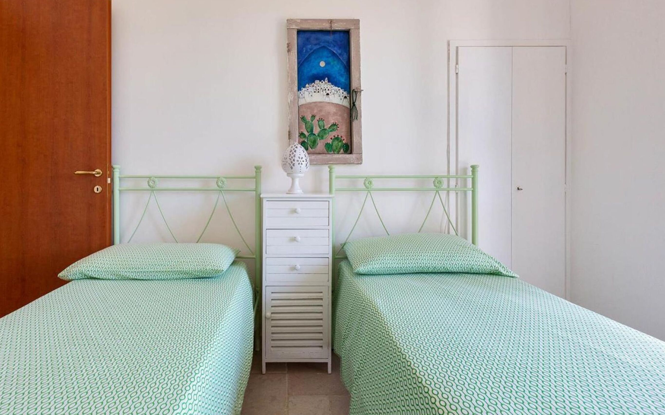 Une chambre avec deux lits simples, une table de chevet, une commode et un tableau représentant une scène nocturne avec un cactus.