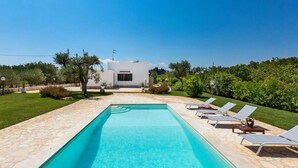 Une piscine avec des chaises longues, un bâtiment blanc et un jardin bien entretenu.